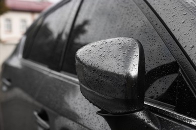 Car with side view mirror in drops of water outdoors, closeup