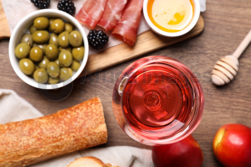 Glass of delicious rose wine and snacks on wooden table, flat lay
