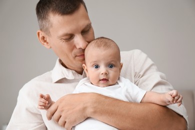 Happy father holding his cute baby on grey background