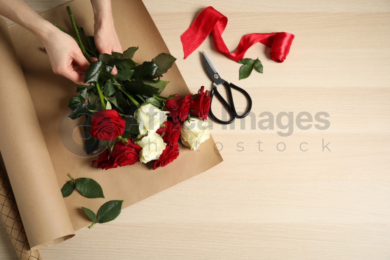 Woman making luxury bouquet of fresh roses at wooden table, top view. Space for text