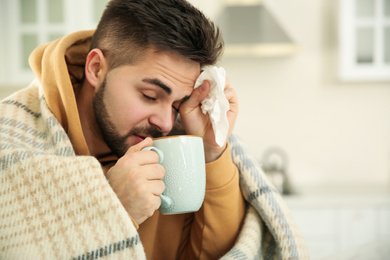 Sick young man with cup of hot drink and tissue at home. Influenza virus