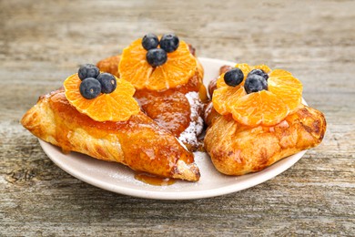 Photo of Fresh tasty puff pastry with sugar powder, jam, tangerines and blueberries on wooden table, closeup