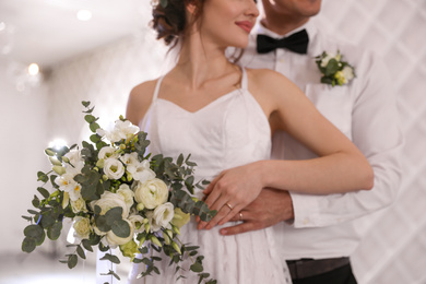Happy newlywed couple with flowers in festive hall, closeup