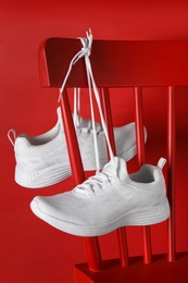 Stylish sneakers with white shoe laces hanging on chair against red background