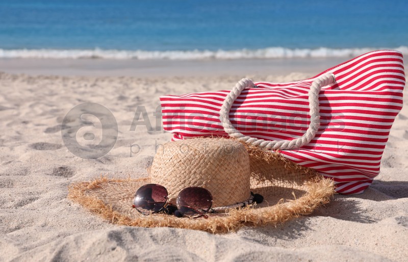 Photo of Straw hat with sunglasses and bag on sandy beach