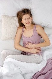 Young woman suffering from abdominal pain in bedroom