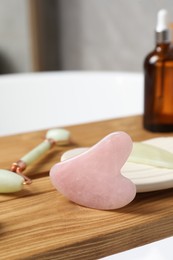 Photo of Jade and rose quartz gua sha tools, natural face roller with cosmetic product on wooden bath caddy, closeup
