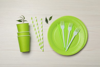 Flat lay composition with disposable tableware and green leaves on white wooden background