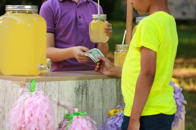 Little boy selling natural lemonade to African-American kid in park, closeup. Summer refreshing drink