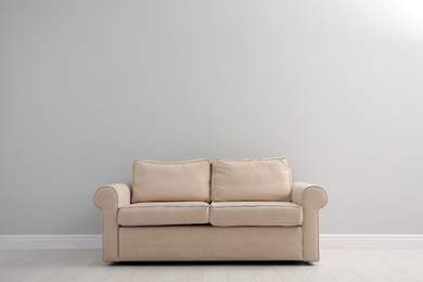 Comfortable beige sofa near light wall indoors, space for text. Simple interior