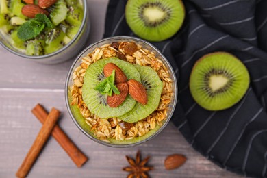 Photo of Delicious dessert with kiwi, muesli and almonds on wooden table, flat lay