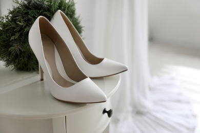 Pair of white high heel shoes, wreath and blurred wedding dress on background, space for text