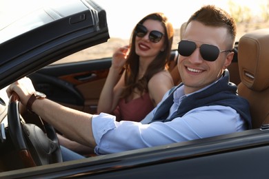 Photo of Stylish couple driving luxury convertible car outdoors