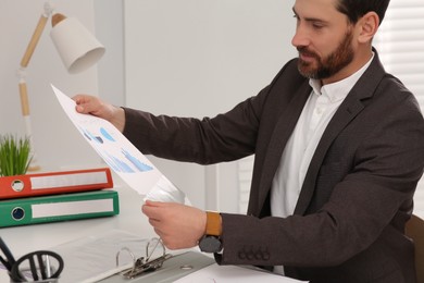 Photo of Businessman putting document into punched pocket at white table in office