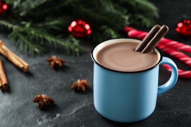 Delicious hot chocolate with cocoa sticks near Christmas decor on black table, closeup. Space for text