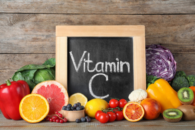 Different products and blackboard with phrase VITAMIN C on wooden table