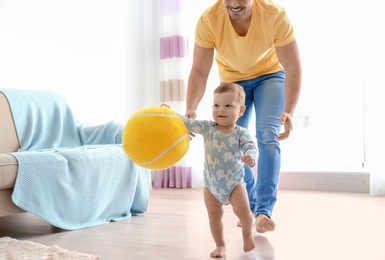 Baby and father playing with ball while learning to walk at home