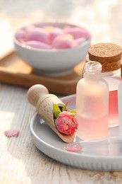 Photo of Bottles of rose essential oil and flowers on white wooden table, closeup
