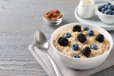 Tasty oatmeal porridge with blackberries and blueberries served on light grey wooden table