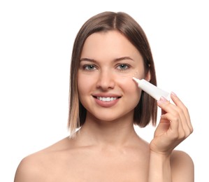 Young woman applying cream under eyes on white background