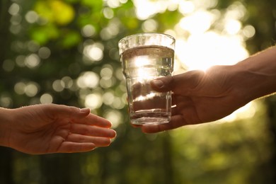 Man giving woman glass of fresh water in forest on sunny day, closeup