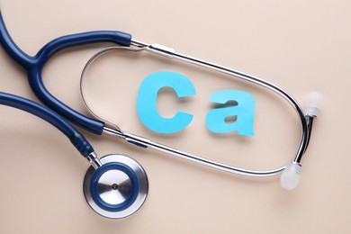 Photo of Stethoscope and calcium symbol made of light blue letters on beige background, flat lay