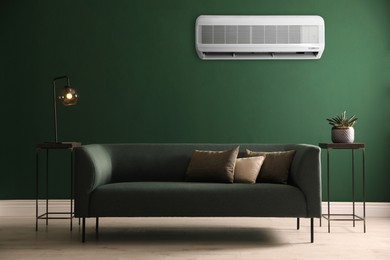Modern air conditioner on green wall in room with stylish sofa