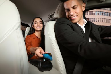 Young woman paying for service using credit card via payment terminal in modern taxi