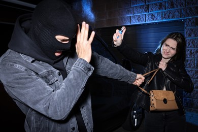 Photo of Woman using pepper spray while thief trying to steal her bag outdoors at night. Self defense concept