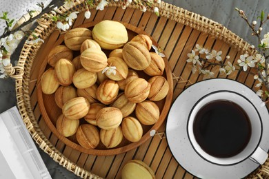 Photo of Delicious walnut shaped cookies with filling, cherry branches and cup of coffee on grey blanket, flat lay. Homemade popular biscuits from childhood