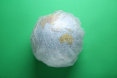 Photo of Globe packed in bubble wrap on light green background, top view. Environmental conservation