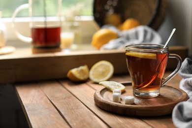 Glass cup with delicious tea, sugar and lemon on wooden table, space for text