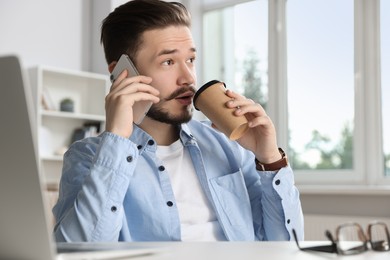 Photo of Man talking on smartphone and drinking coffee in office