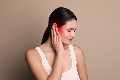 Woman suffering from ear pain on beige background