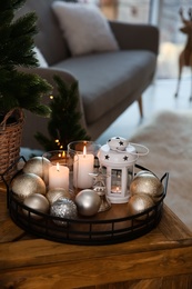 Photo of Burning candles, lantern and Christmas balls on wooden table indoors