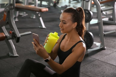 Portrait of athletic woman with protein shake and smartphone in gym
