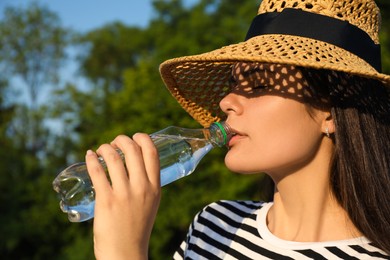 Photo of Young woman in straw hat drinking water outdoors on hot summer day. Refreshing drink