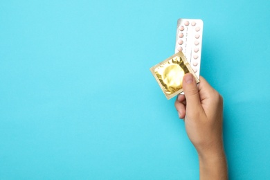 Woman holding condom and birth control pills on blue background, top view with space for text. Safe sex