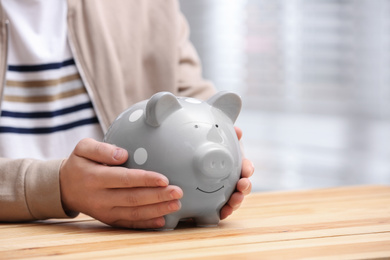 Man with piggy bank at wooden table, closeup