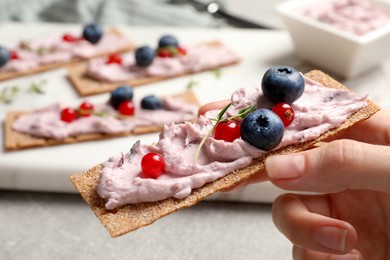 Woman holding tasty cracker sandwich with cream cheese, blueberries, red currants and thyme at table, closeup