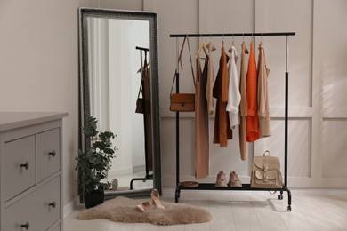 Rack with stylish women's clothes and mirror in dressing room