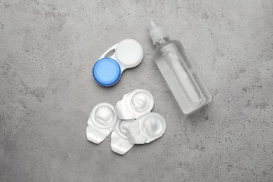 Photo of Packages with contact lenses, case and drops on grey table, flat lay