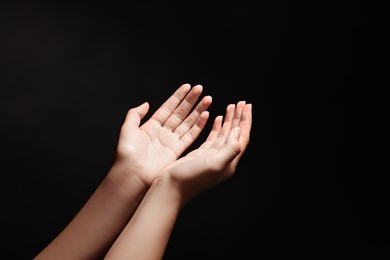 Woman stretching hands towards light in darkness, closeup