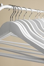 White clothes hangers on metal rail against beige background, closeup
