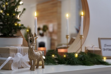Decorative reindeer near gift box on shelf with Christmas decor. Interior design