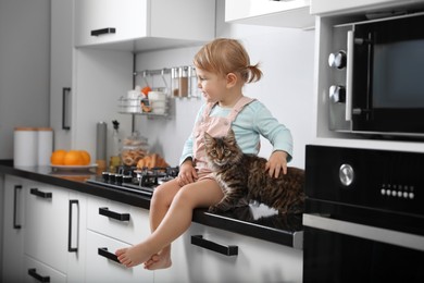 Cute little child sitting with adorable pet on countertop in kitchen