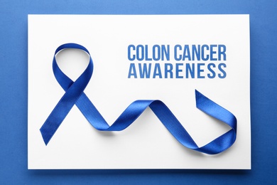 Card with words COLON CANCER AWARENESS and blue ribbon on color background, top view