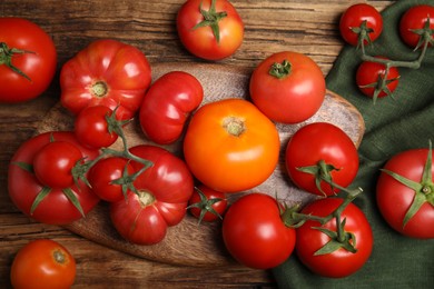 Photo of Many different ripe tomatoes on wooden table, flat lay