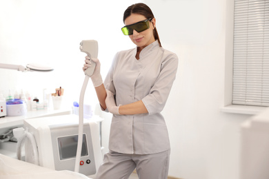 Photo of Young woman holding professional laser epilator in beauty salon