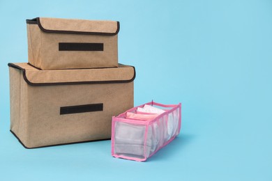 Textile storage cases and organizer with folded clothes on light blue background. Space for text